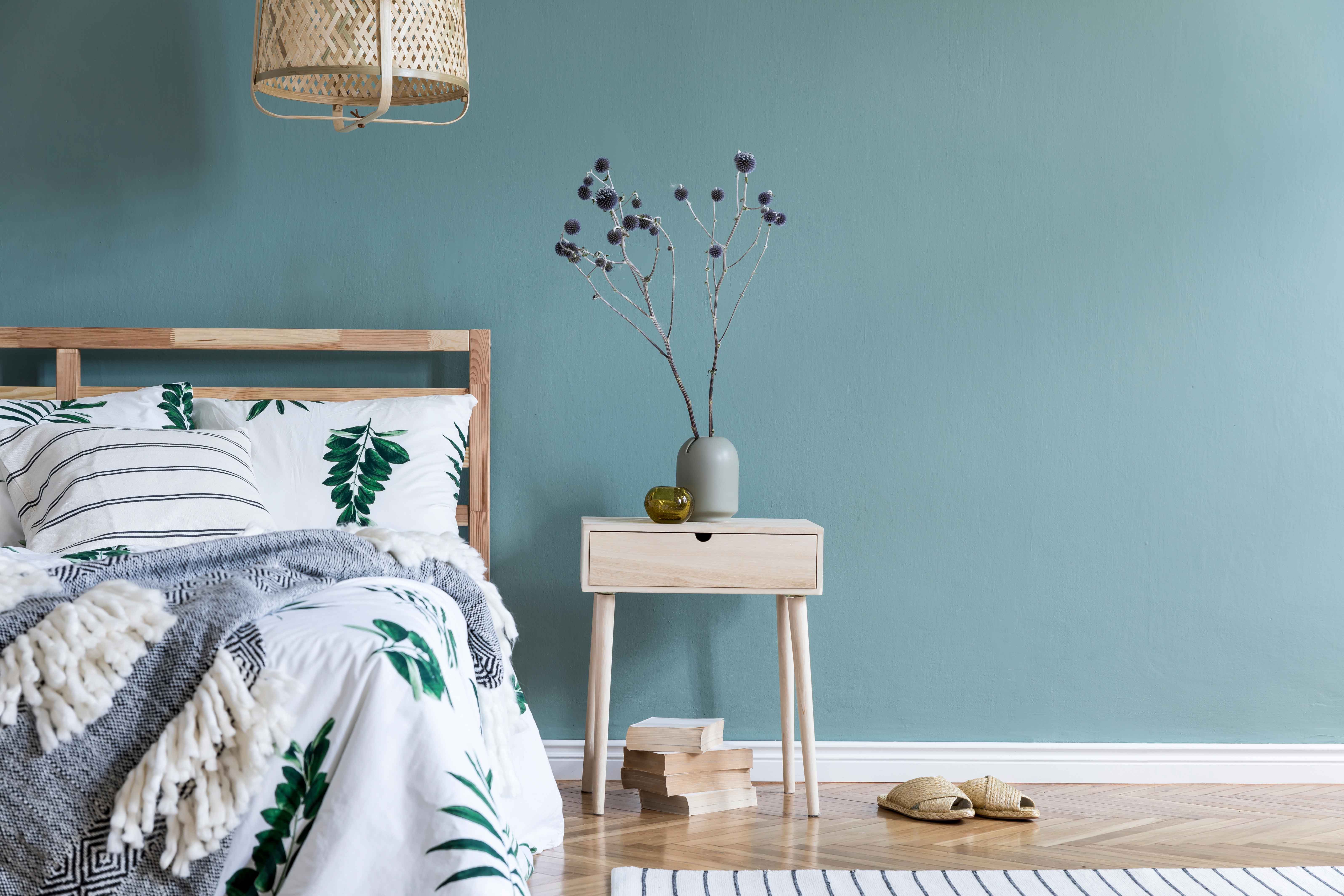 minimalistic-composition-of-bedroom-interior-with-wooden-bed-shelf-flowers-in-vase-rattan-lamp-books-and-elegant-accessories